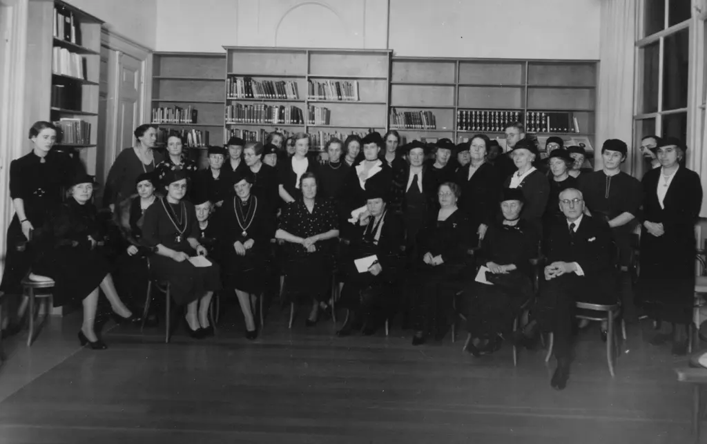 Groep van voornamelijke vrouwen zitten en staan voor een aantal boekenkasten
