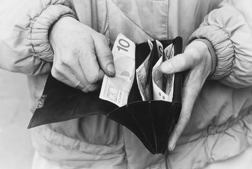 Twee handen houden een portemonnee met geld vast. In de portemonnee zit een briefje van 10 gulden.